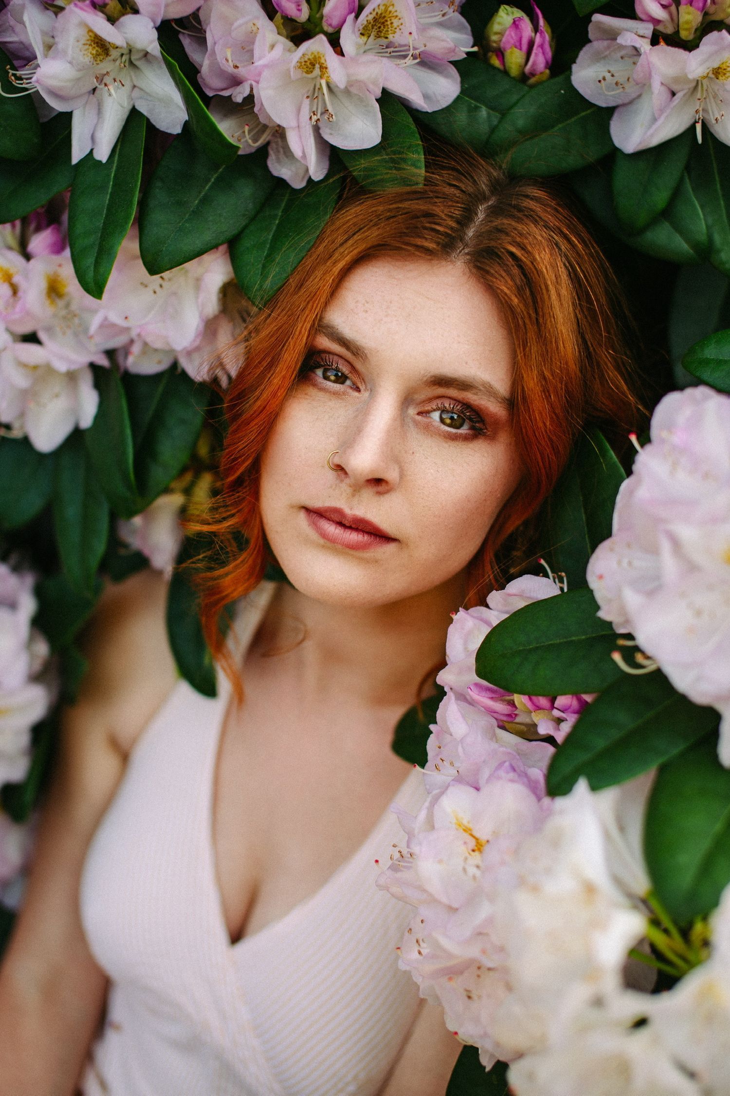 Frau liegt verträumt zwischen Rhododendron-Blüten und schaut in die Kamera – Portraitfotografie Julia Kippes in Bielefeld