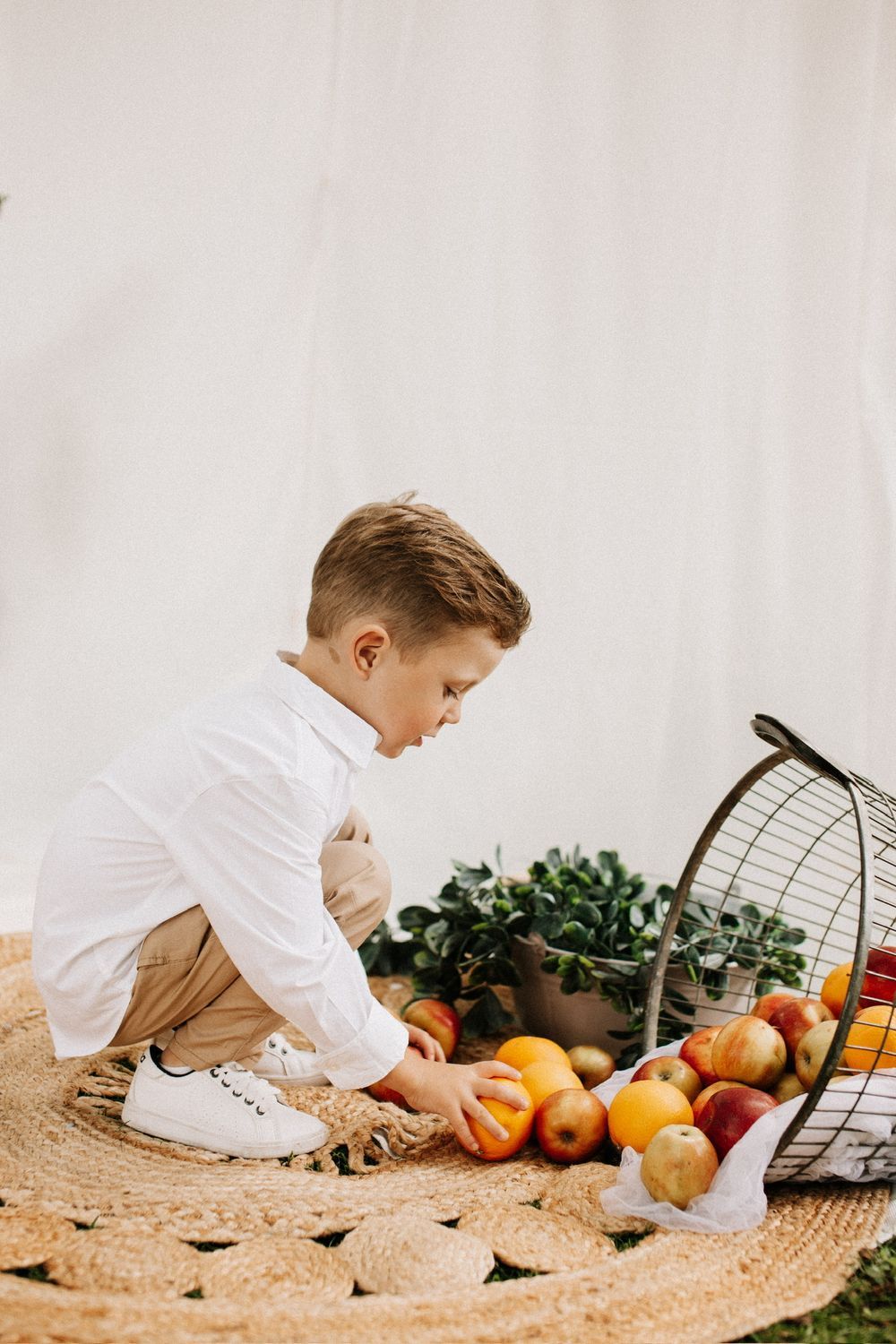 Kleiner Junge in weißem Hemd spielt mit Früchten aus umgekipptem Korb – Familien-Studiofotografie Julia Kippes