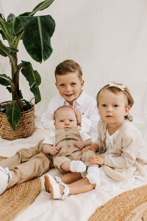 Geschwister in Beige und Weiß sitzen zusammen in einem Boho-Setting – Geschwisterfotografie Julia Kippes