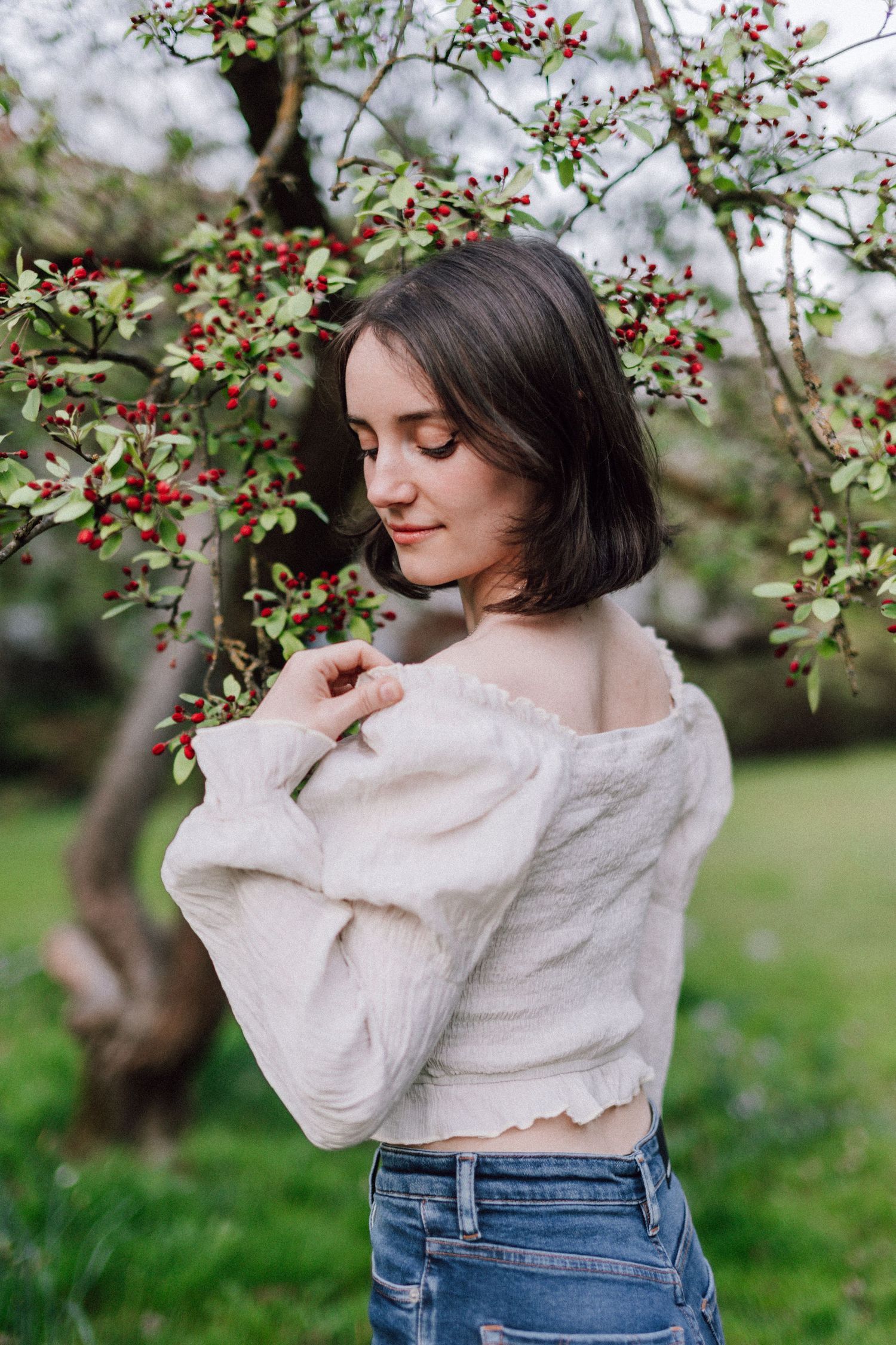 Frau steht vor einem blühenden Kirschbaum und schaut verträumt über ihre Schulter – Portraitshooting Julia Kippes
