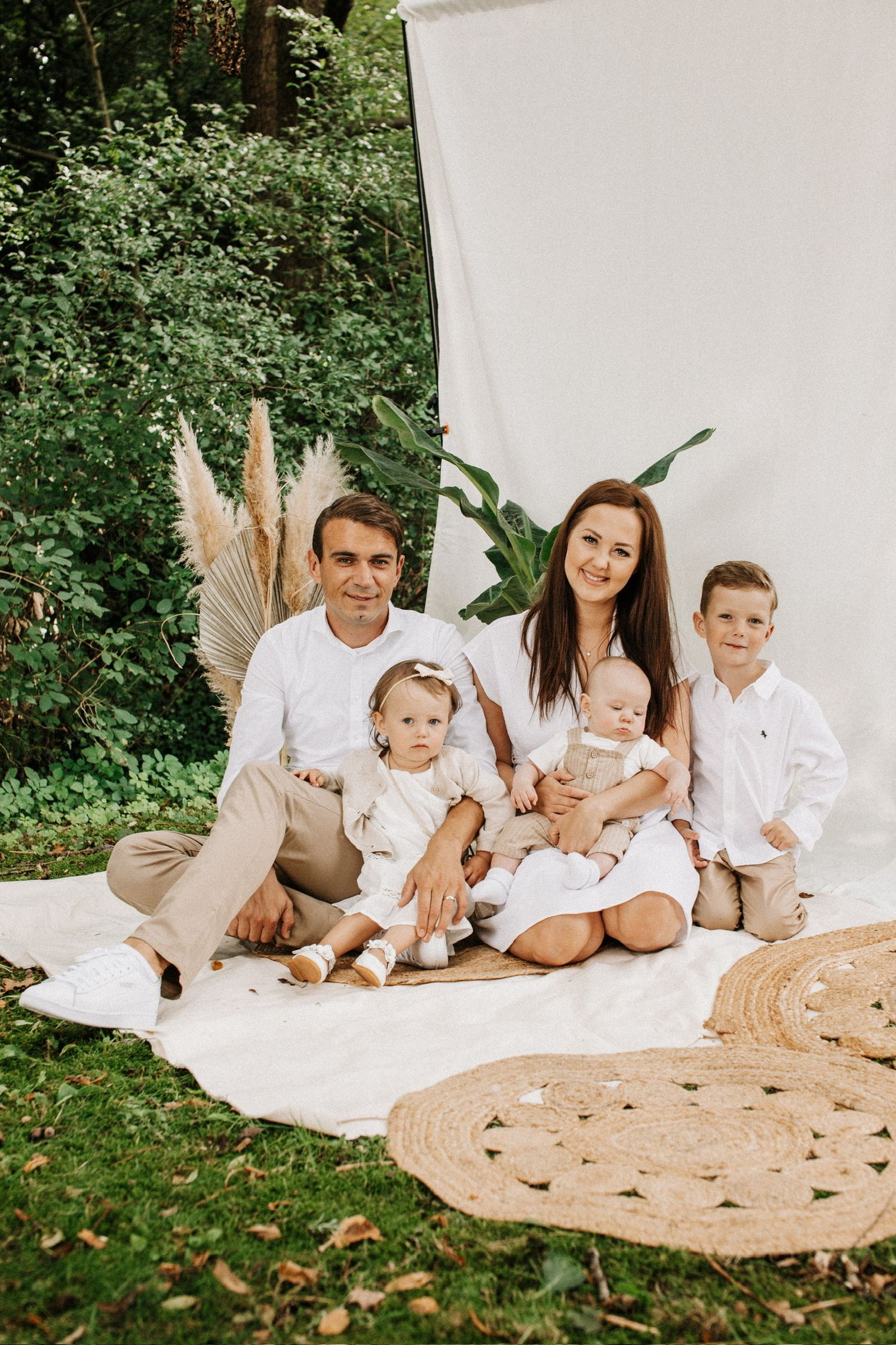 Familie gekleidet in beige und weiß sitzt in einem Boho Setting draußen